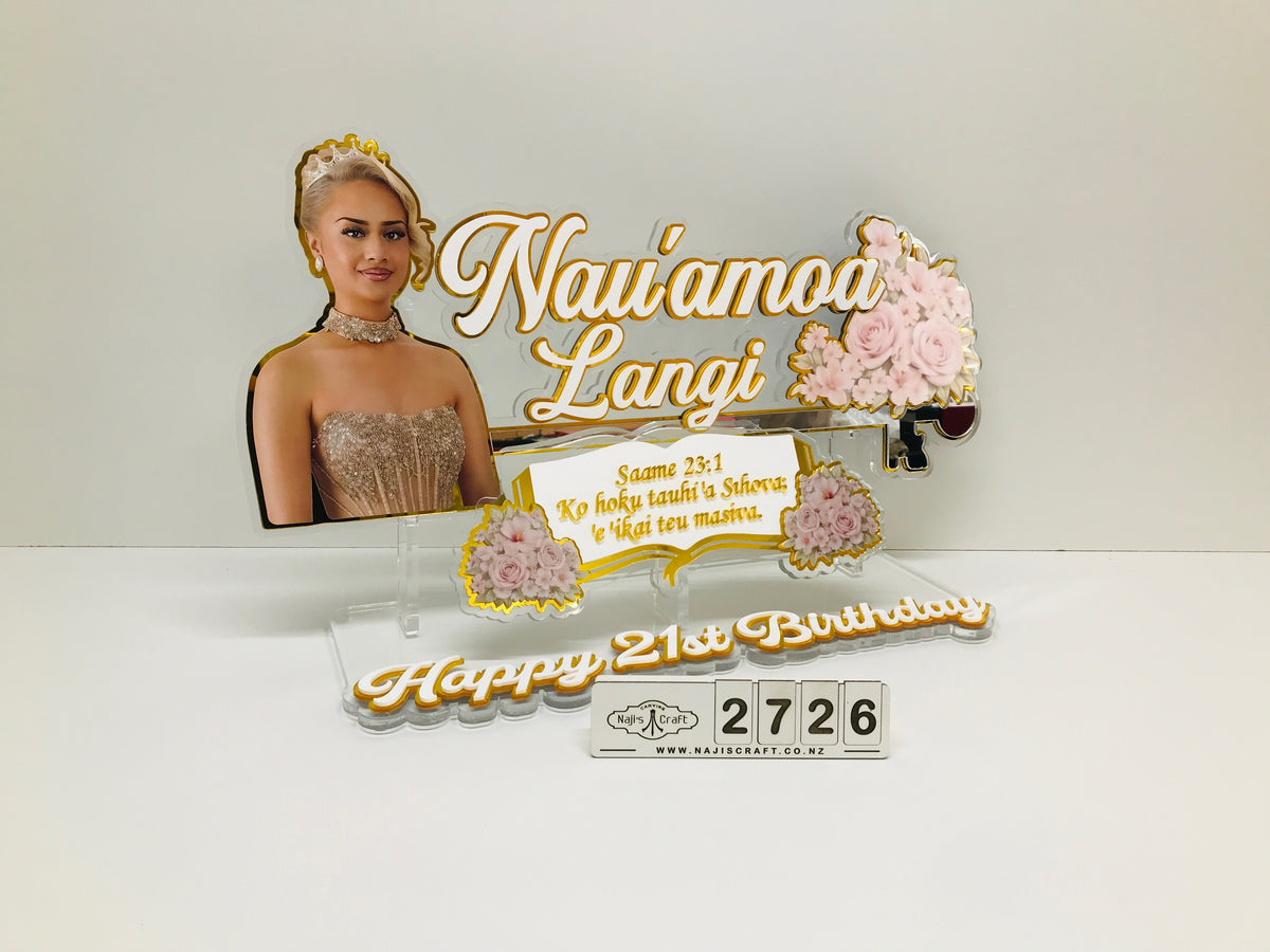 A custom acrylic birthday cake topper stand featuring a photo of a woman, the text 'Nau'amoa Langi', a Bible verse, pink roses, and a 'Happy 21st Birthday' message with a countdown timer, displayed on a white background.